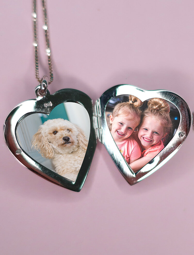 Heart shaped locket containing photos of two children and a dog on a pink background