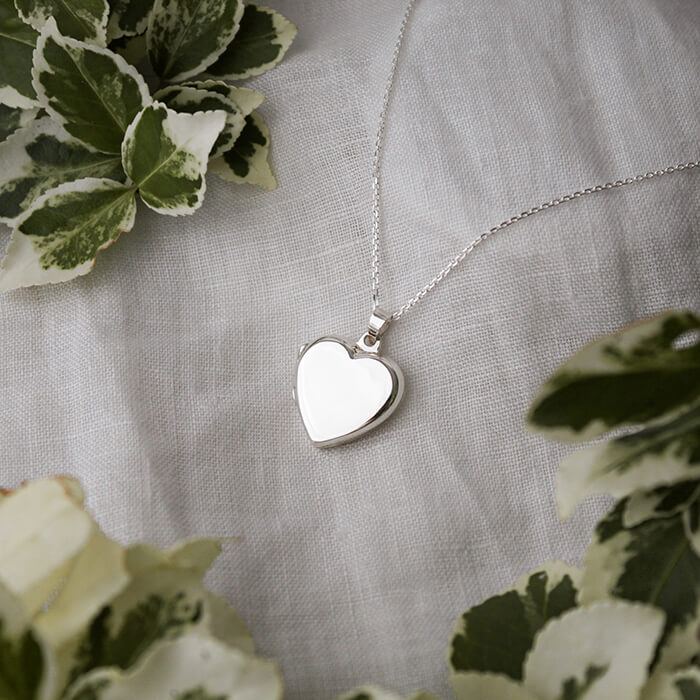 Delicate sterling silver heart shaped locket ona linen background with greenery.
