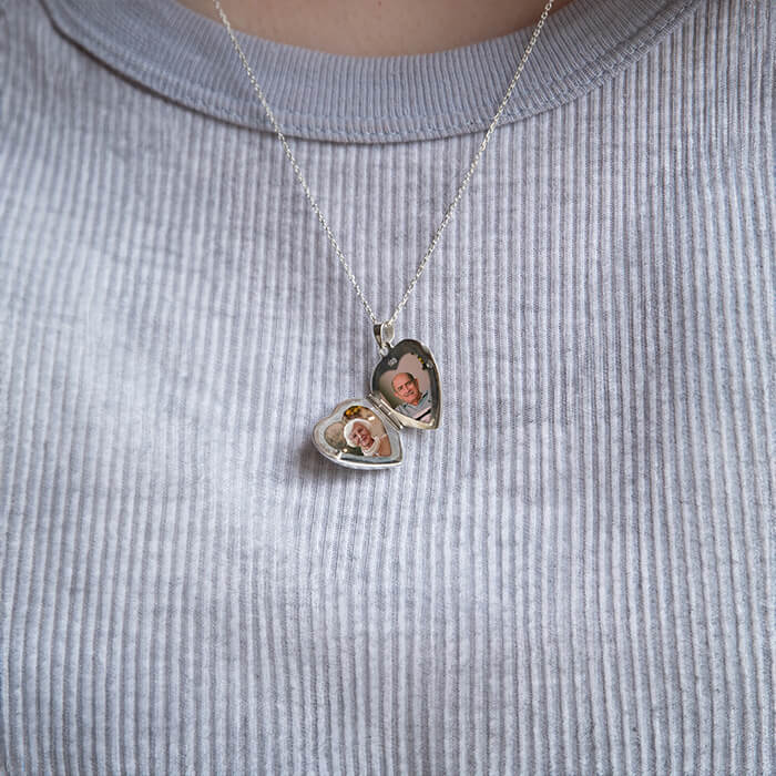 Open silver heart locket showing two photos contained within on a blue background.