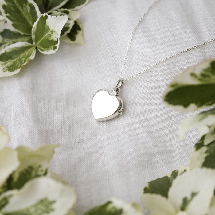 small sterling silver heart shaped locket on a white linen background