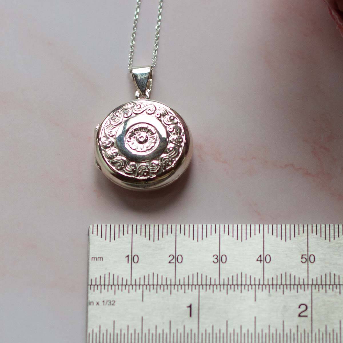 Large silver locket with a ruler showing 20mm on a pink background. The locket is round.