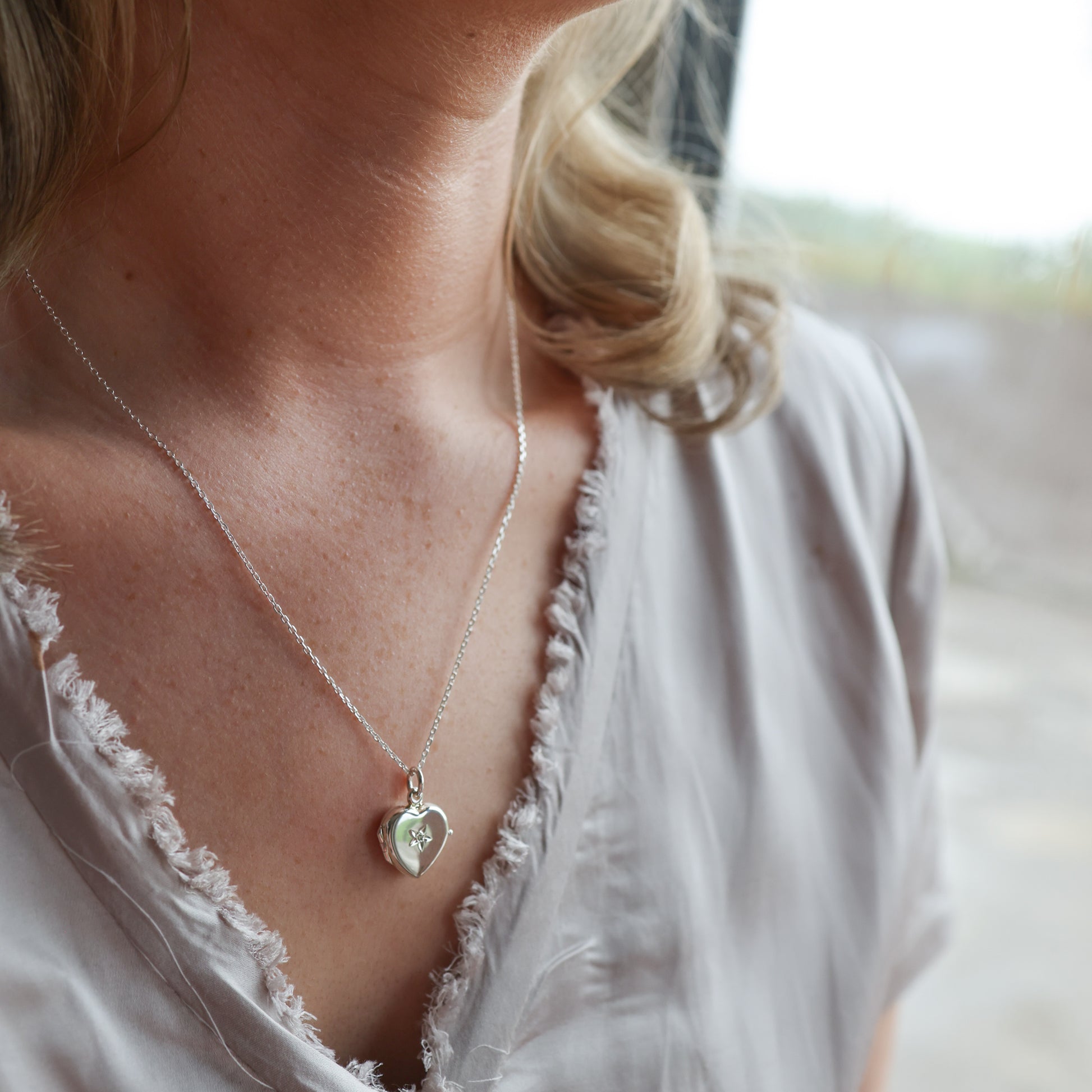 Model wearing heart shaped locket with diamond. Wearing a grey top.