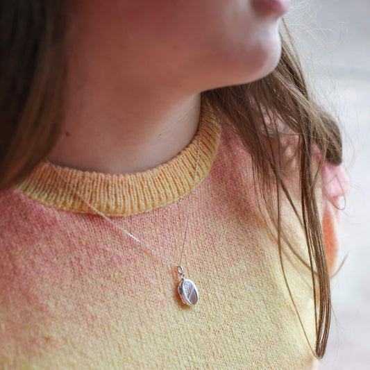 Girls wearing oval silver locket with photos and wearing a yellow and orange sweater