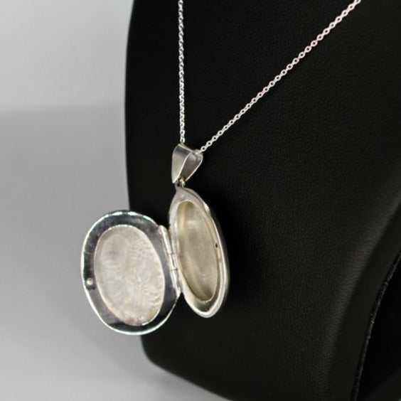 Oval shaped embellished silver photo locket necklace with white mother of pearl inlay on Italian silver chain displayed on black bust.