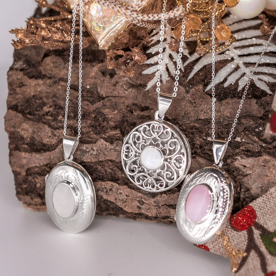 Oval shaped embellished silver photo locket necklace with white mother of pearl inlay on Italian silver chain and a round photo locket necklace and an oval with pink photo locket necklace on a Christmas log.
