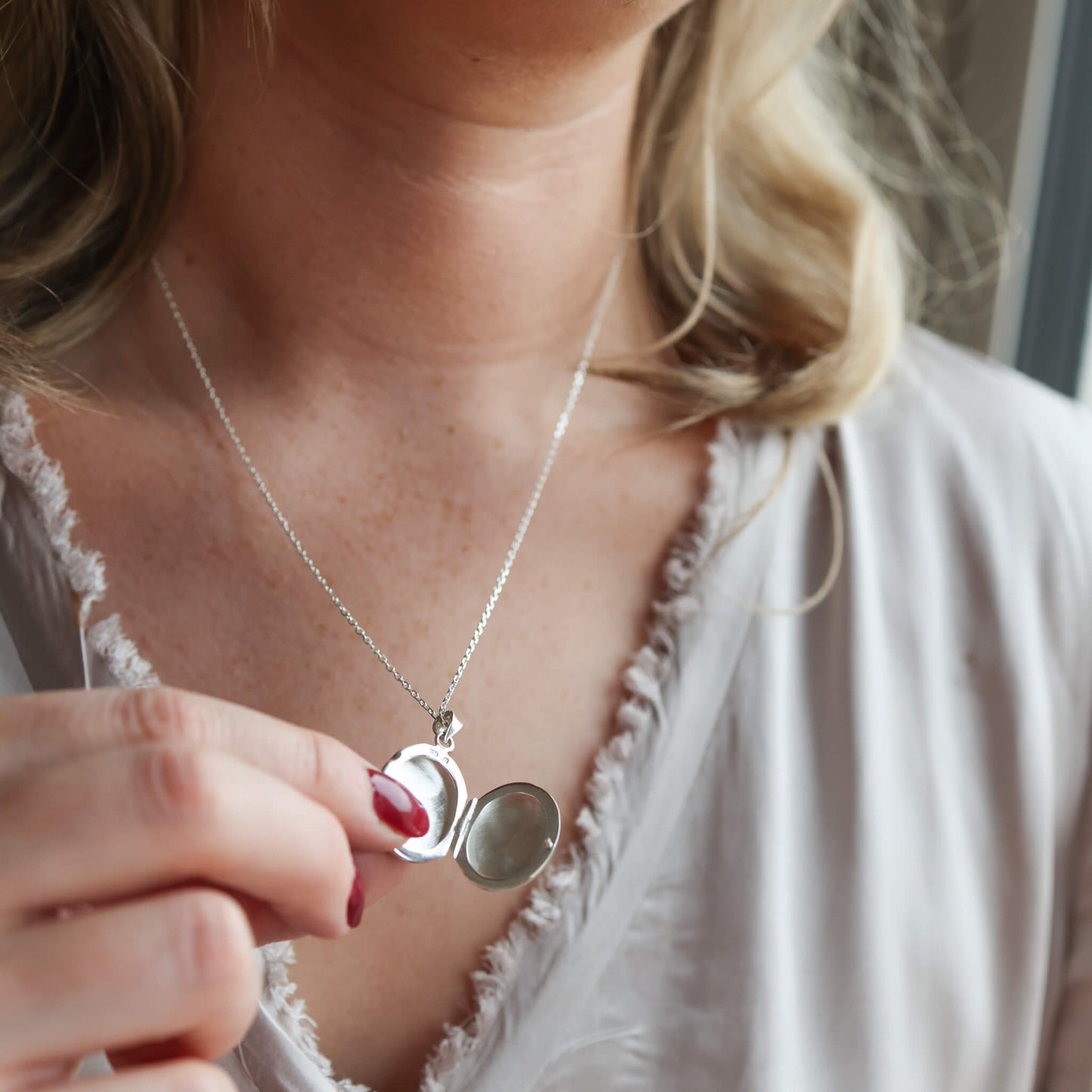 Model wearing grey top holding an open oval locket