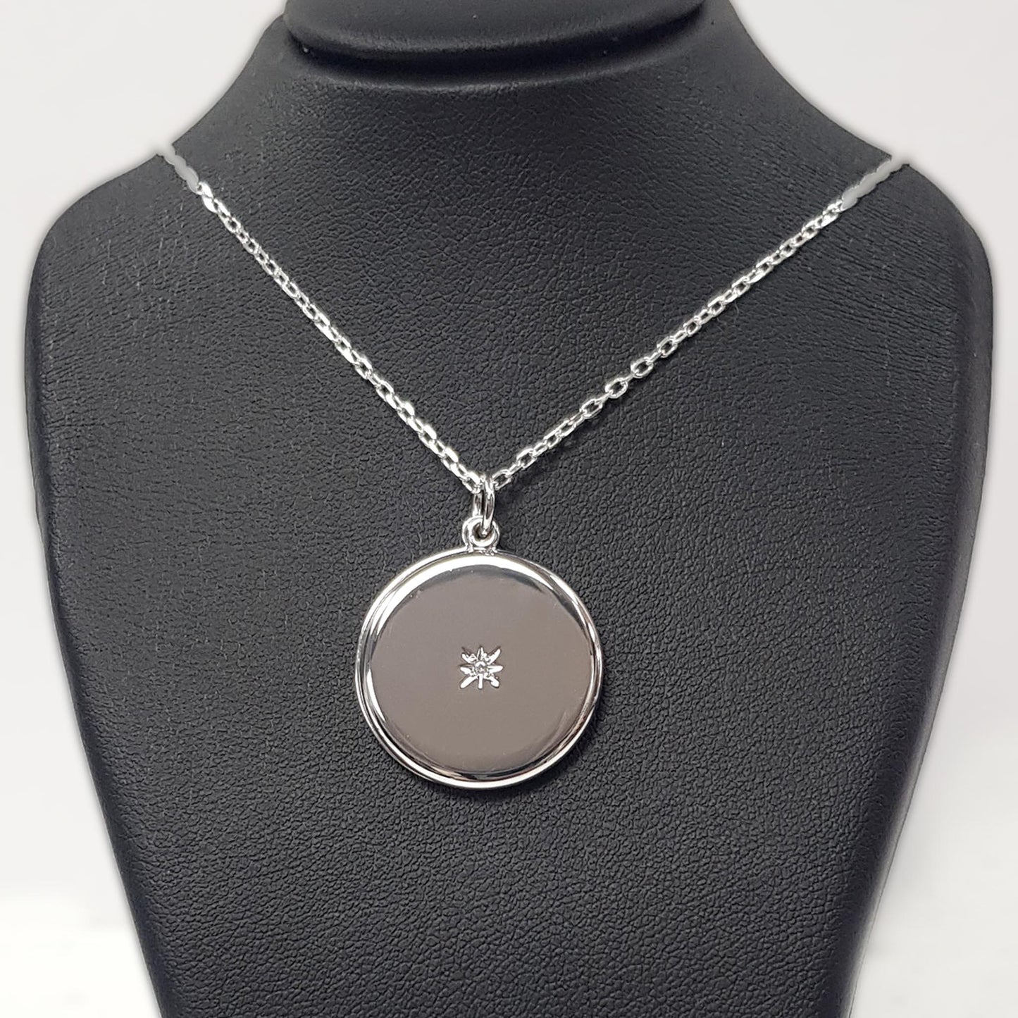 Round sterling silver locket with chain photographed on a black bust
