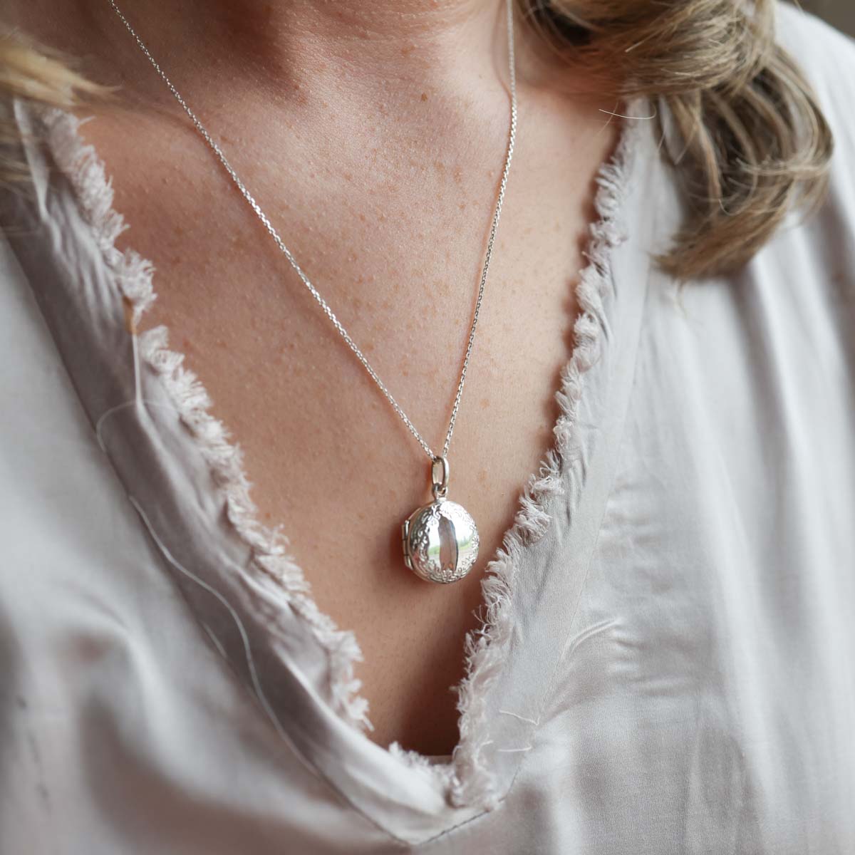 Model wearing grey top with round locket necklace on a chain