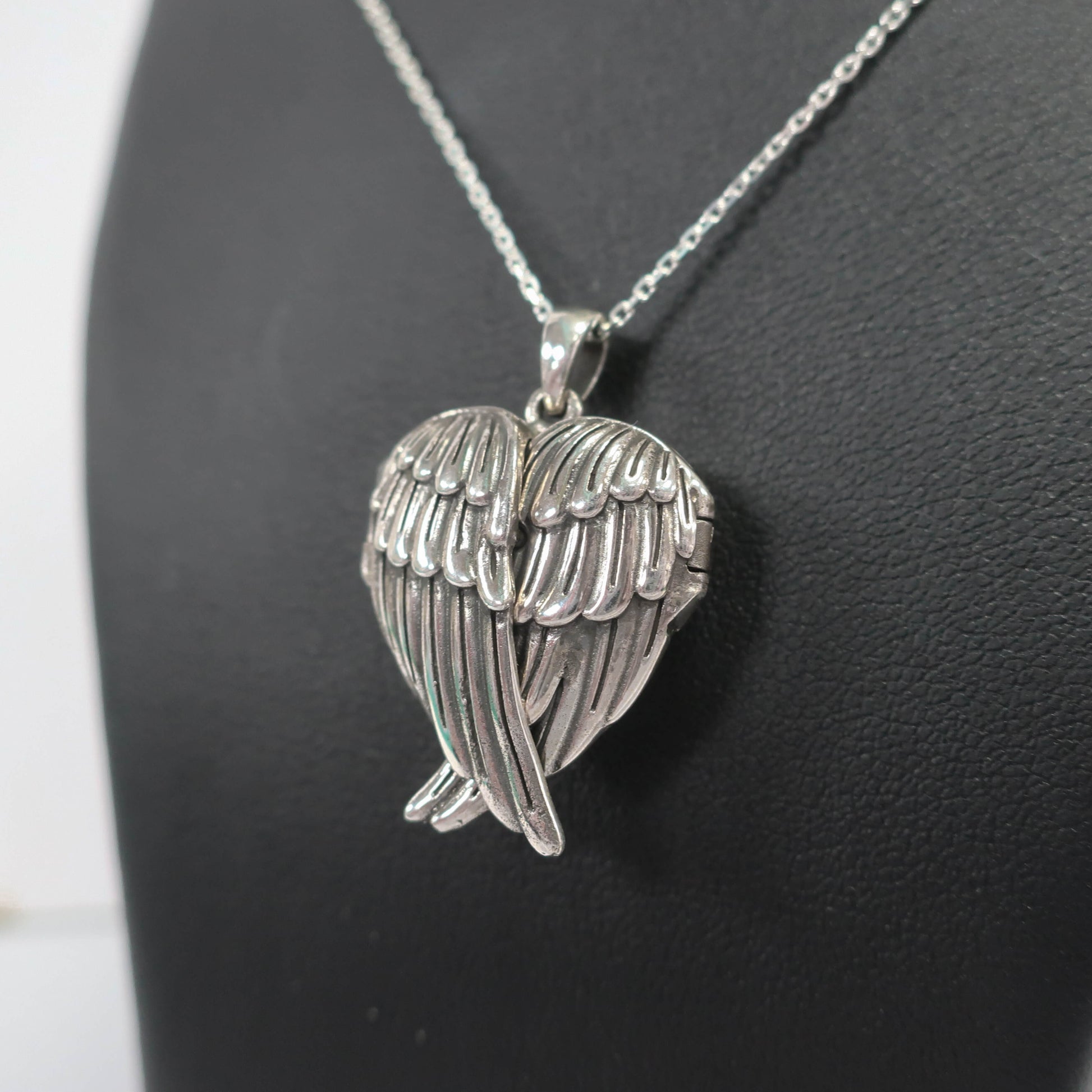 Silver wing-shaped pendant on a chain against a dark background