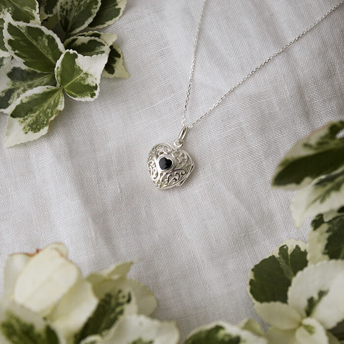 Silver locket necklace with a heart-shaped pendant on a light fabric background with green leaves.
