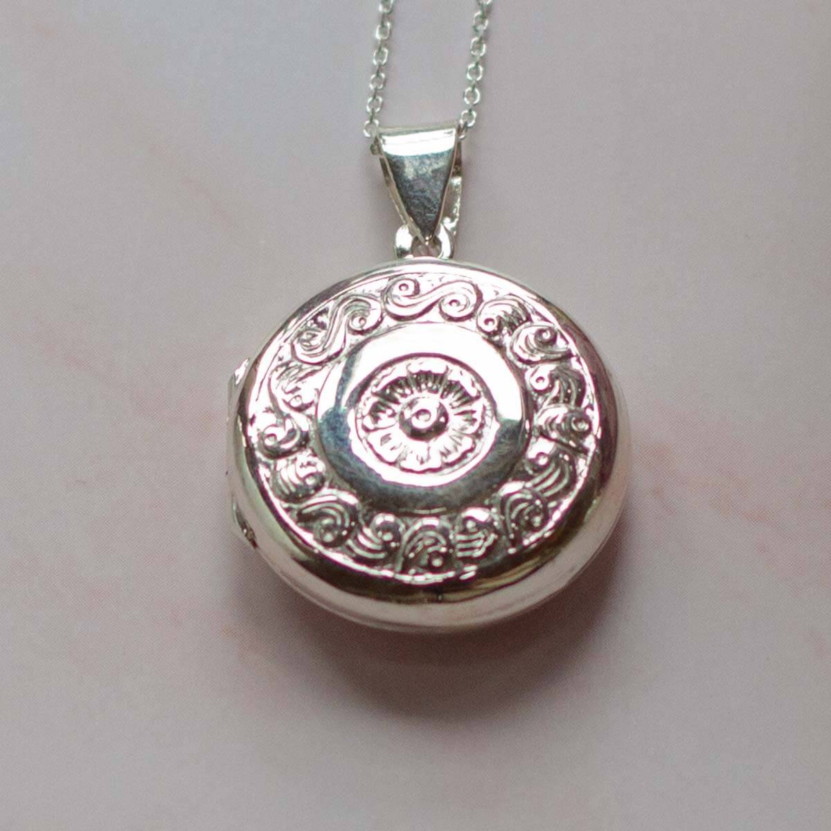 Large silver locket, round in shape on a pale pink background.