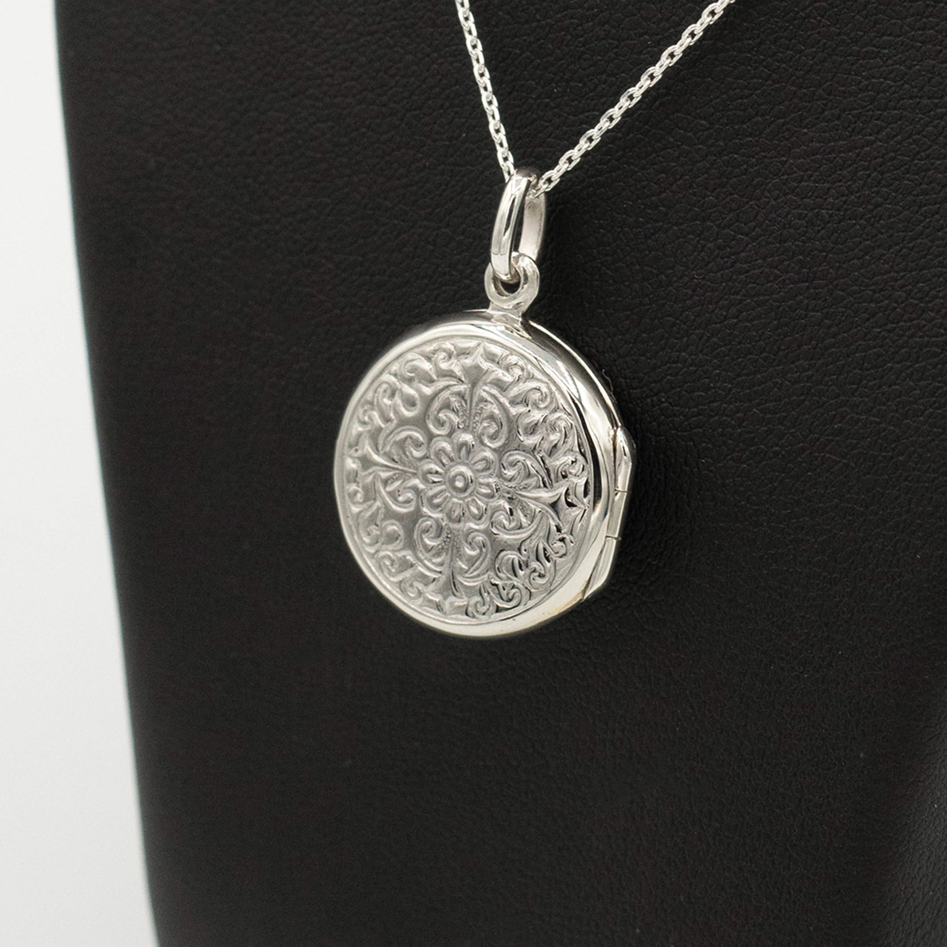side on view of sterling silver round shaped locket with intricate ornate design