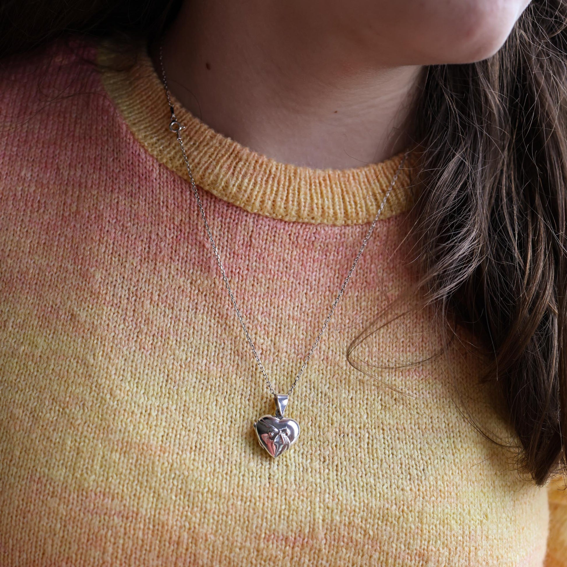 Child wearing a heart shaped locket with a bow embellishment wearing an orange and pink sweater