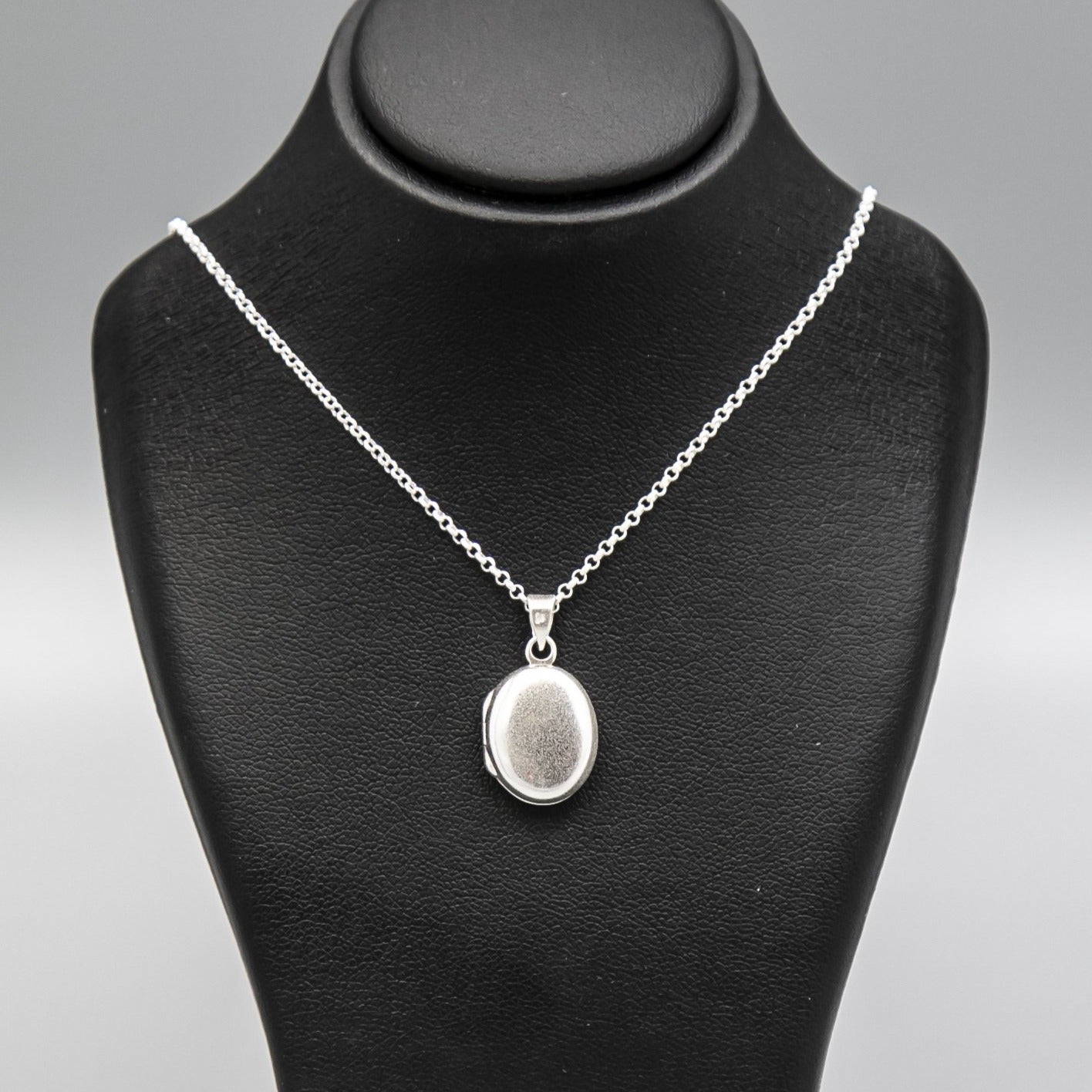 Small silver locket necklace on silver chain displayed on black bust