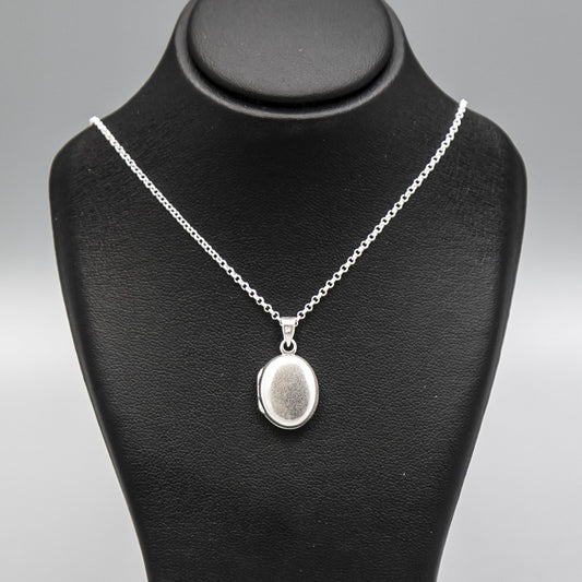 Small silver locket necklace on silver chain displayed on black bust