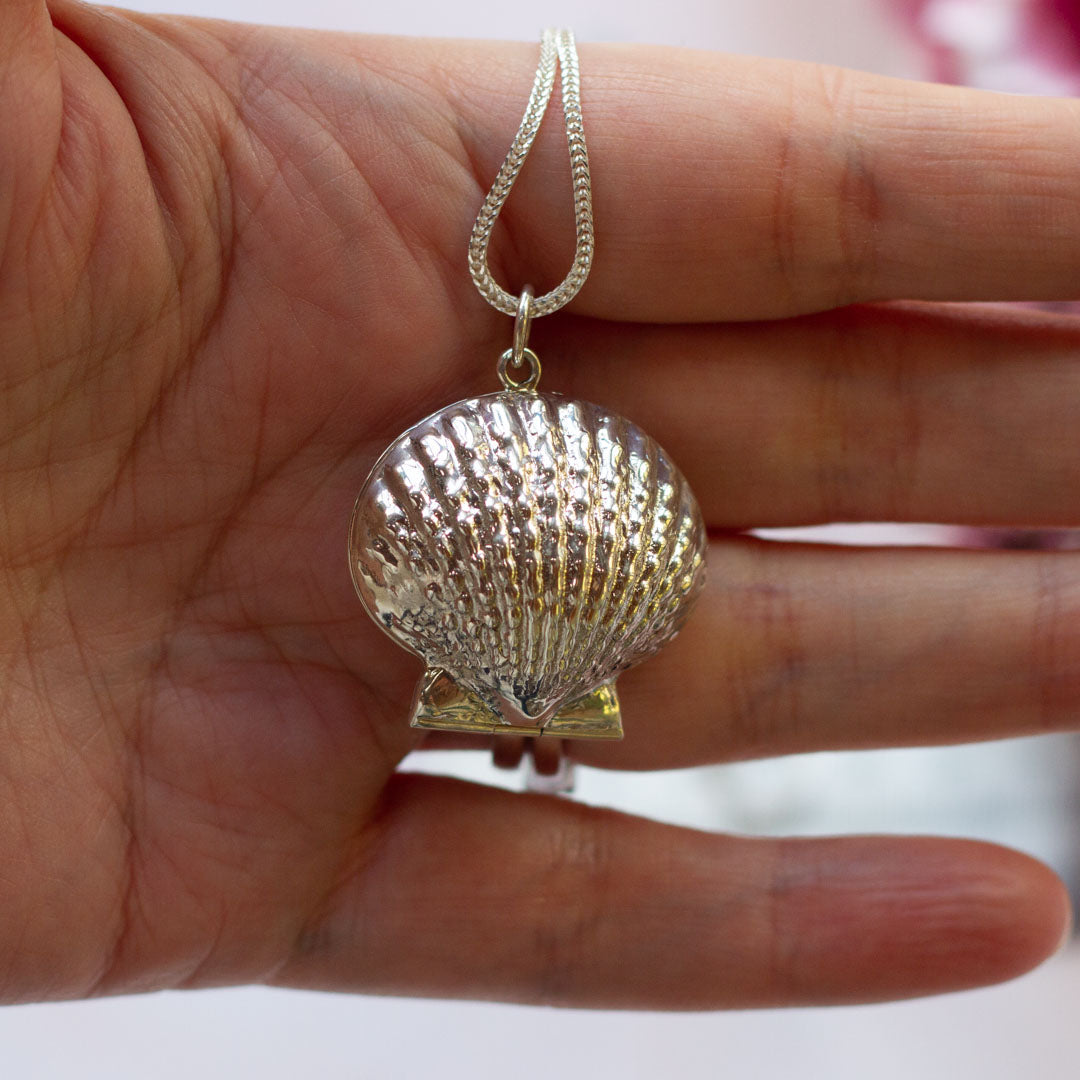 Shell shaped photo locket necklace shown against ladies hand