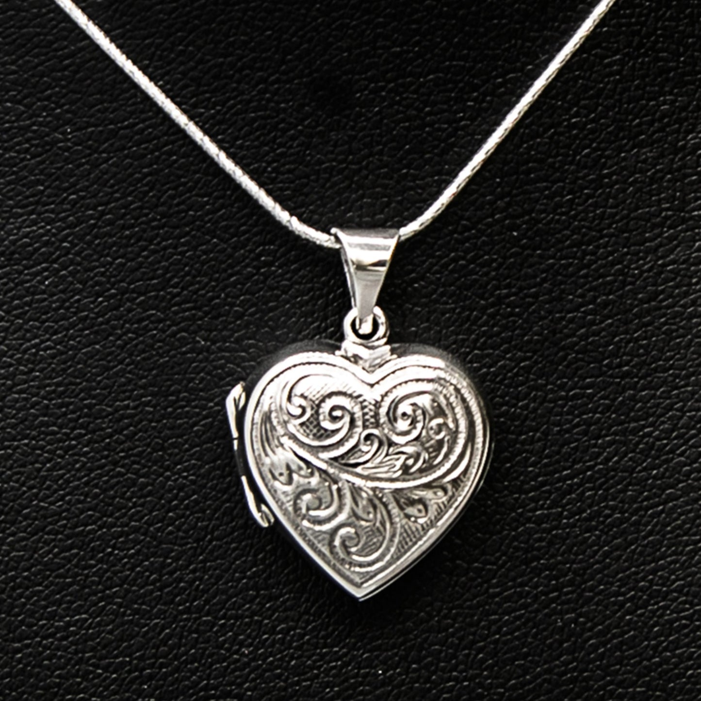 Silver heart-shaped photo locket pendant with embellishment on silver chain displayed on black