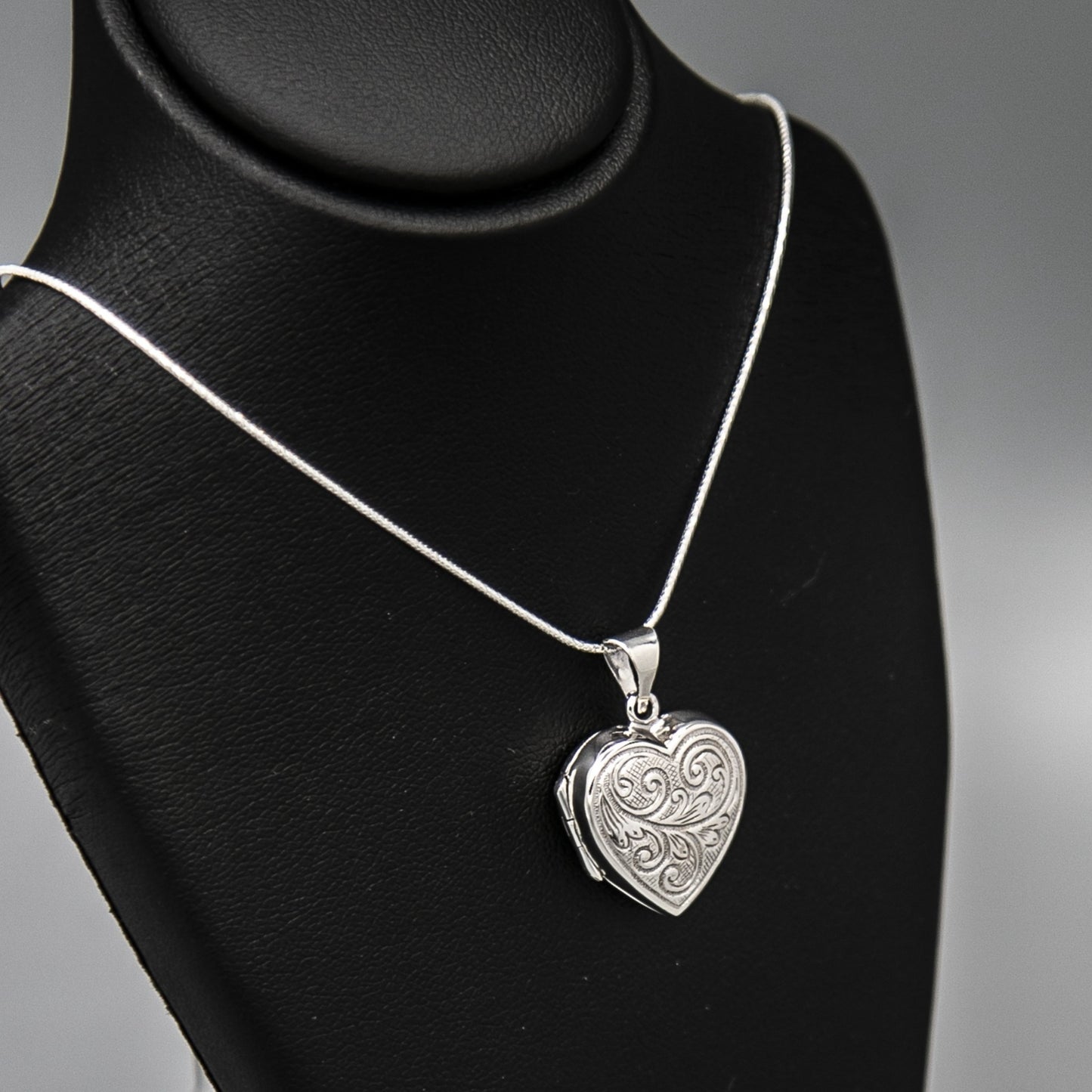 Silver heart-shaped photo locket pendant with embellishment on silver chain displayed on black
