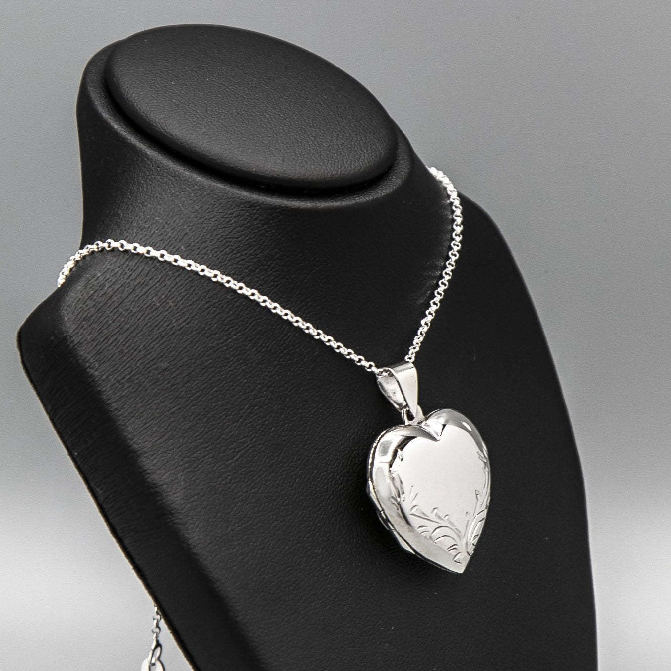 Large silver heart shaped photo locket necklace on silver chain displayed on a black bust.