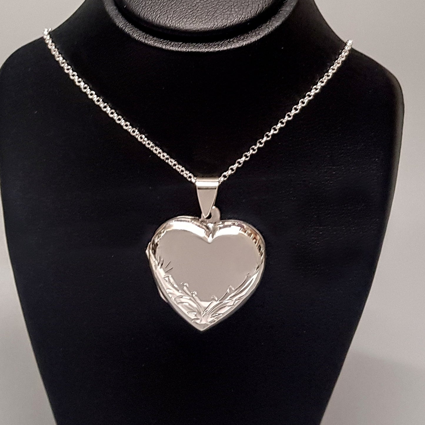 Large silver heart shaped photo locket necklace on silver chain displayed on a black bust.