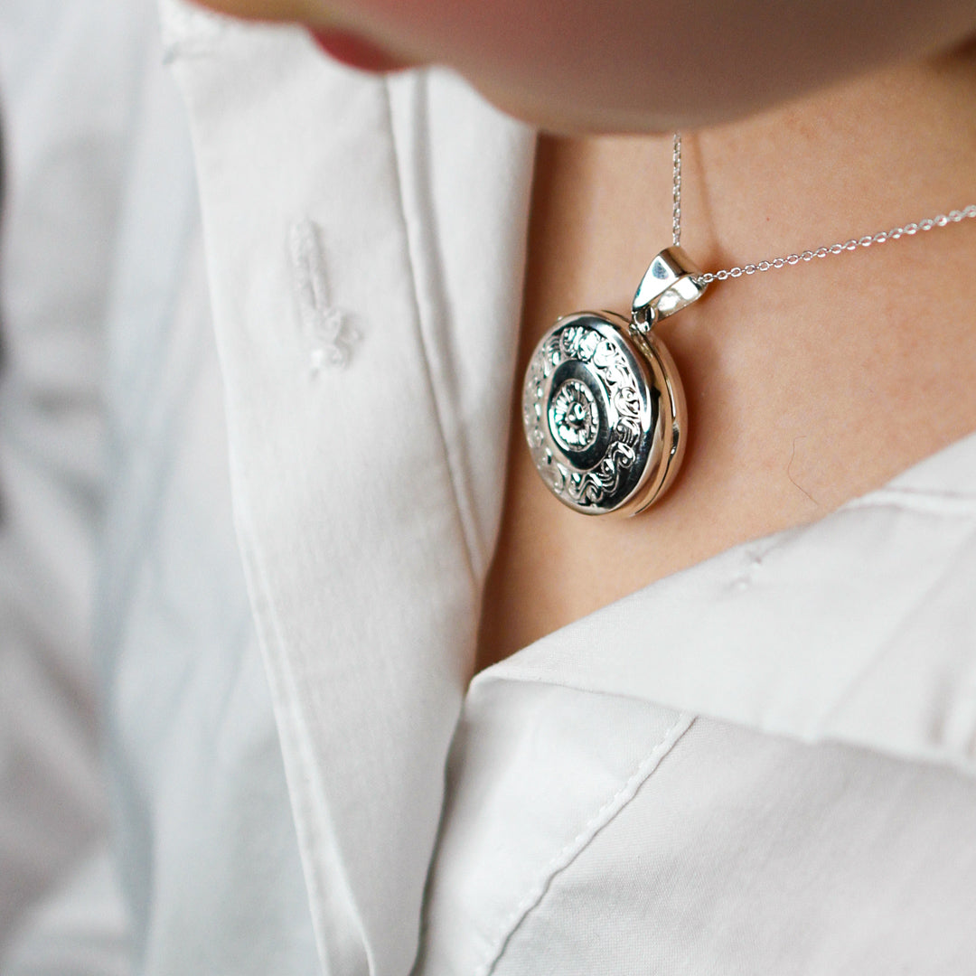Model wears white shirt and Large silver locket pendant on a silver chain.