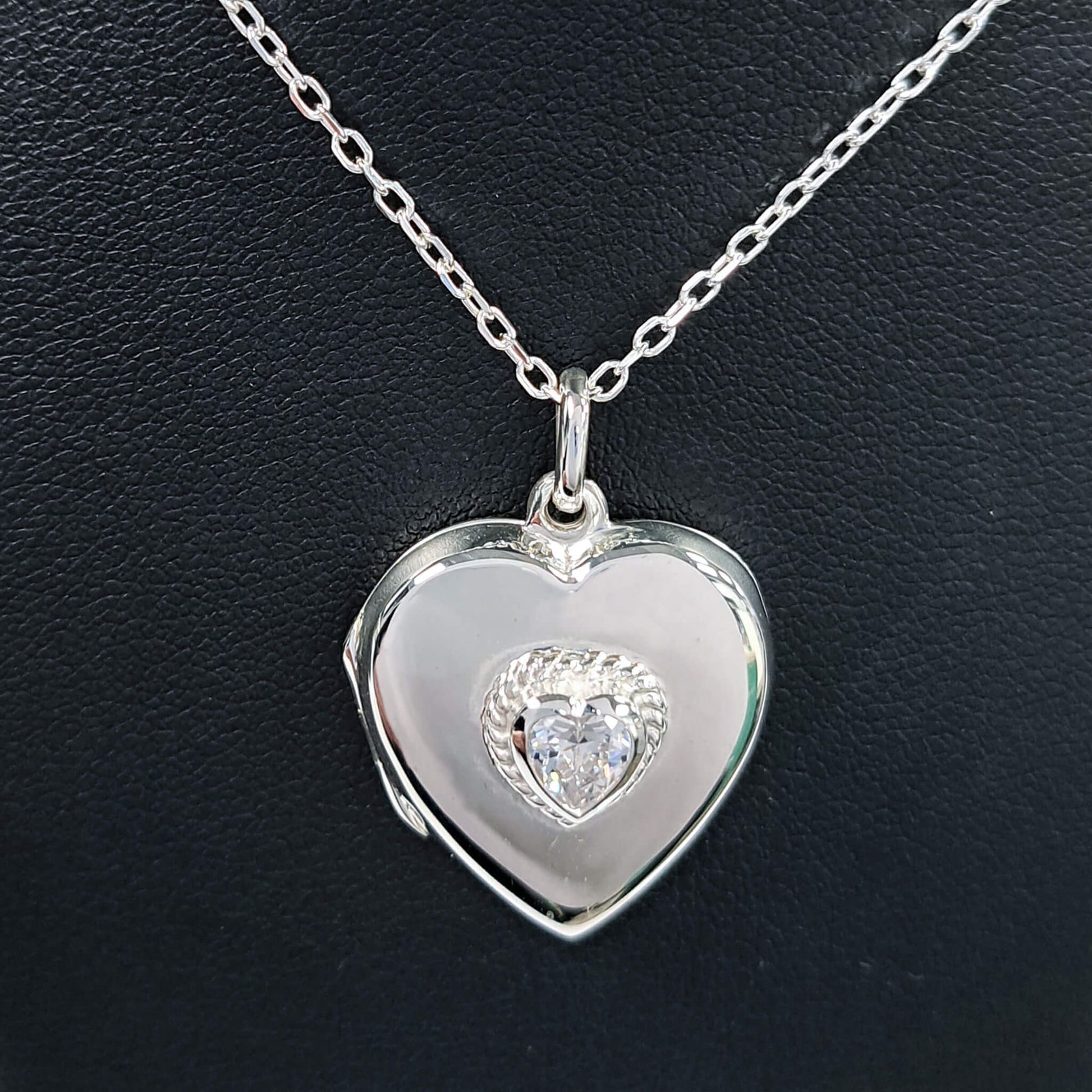 Close up of Heart-shaped chain and locket necklace with cubic zirconia inset on a silver chain.