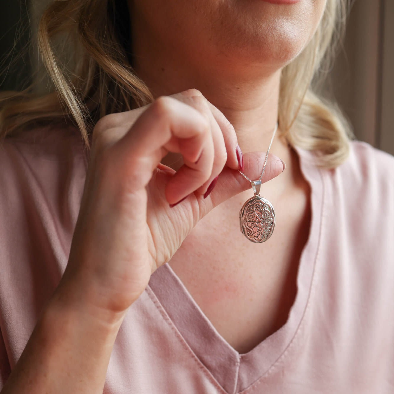 Model wearing pink top holding up oval photo locket