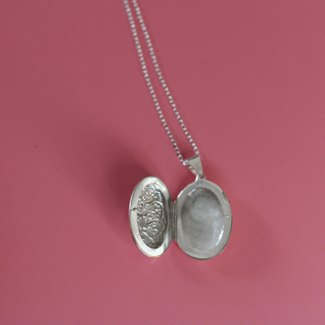Ornate oval photo locket necklace on a pink background